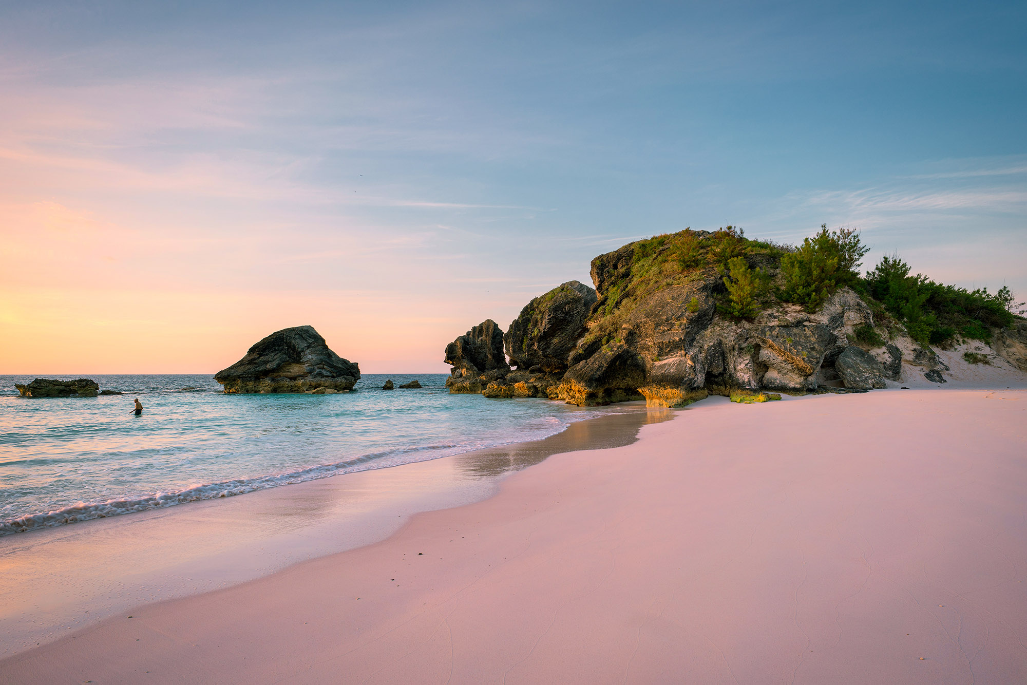A small pink hotel building on a white sand beach next to the sea
