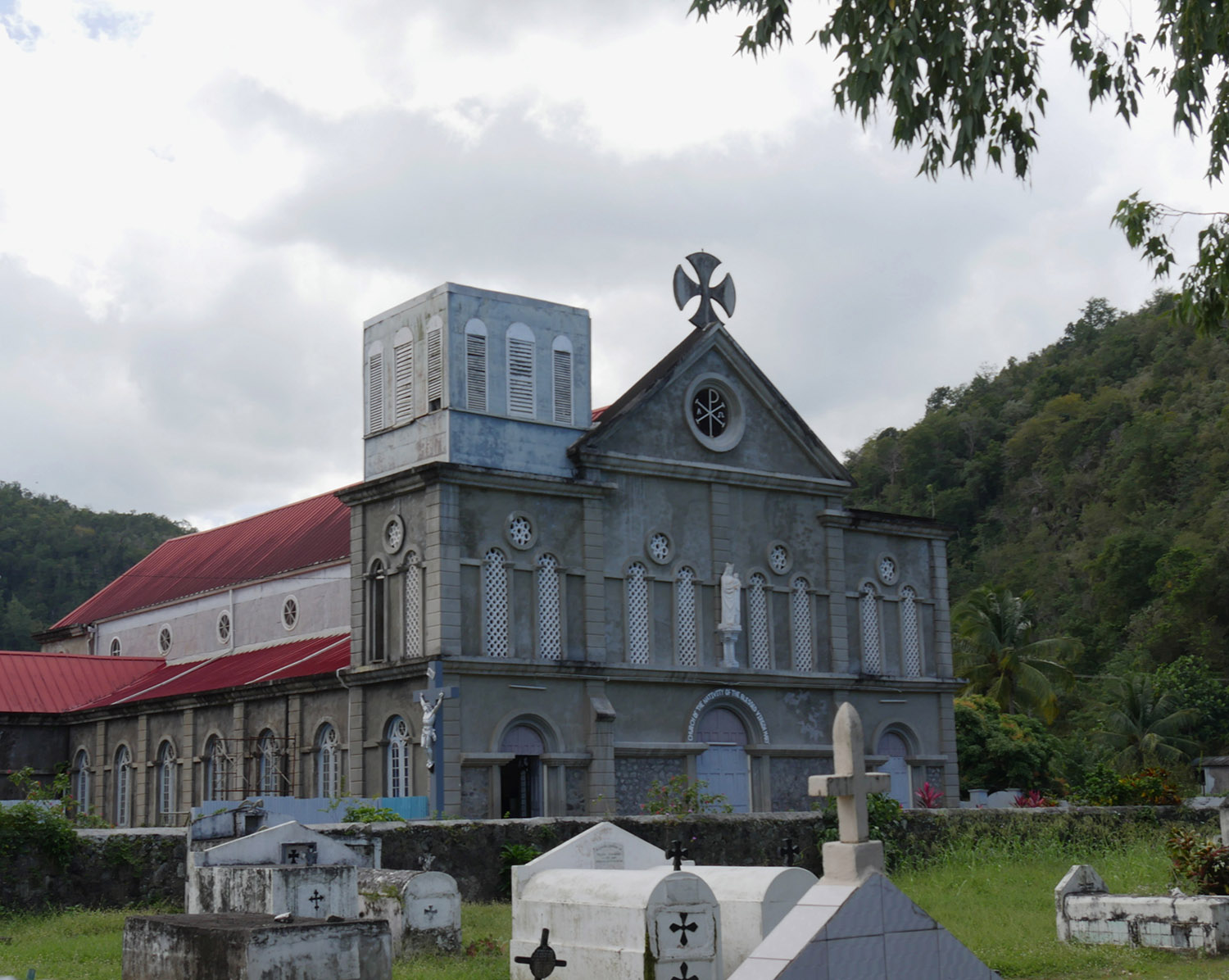 Exterior of Church Of Assumption and graveyard surrounded by tropical forest