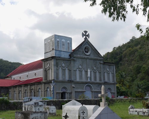 Exterior of Church Of Assumption and graveyard surrounded by tropical forest