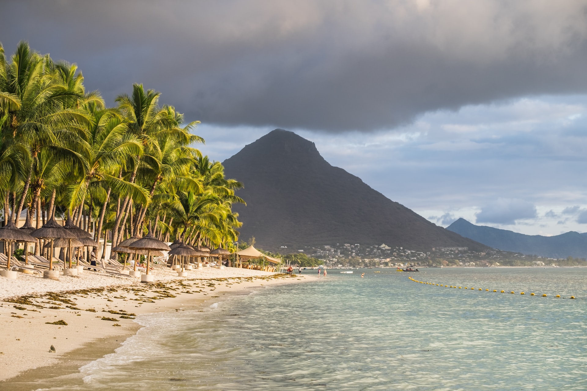 Straw Umbrellas And Sun Beds Lined Up On narrow tropical beach