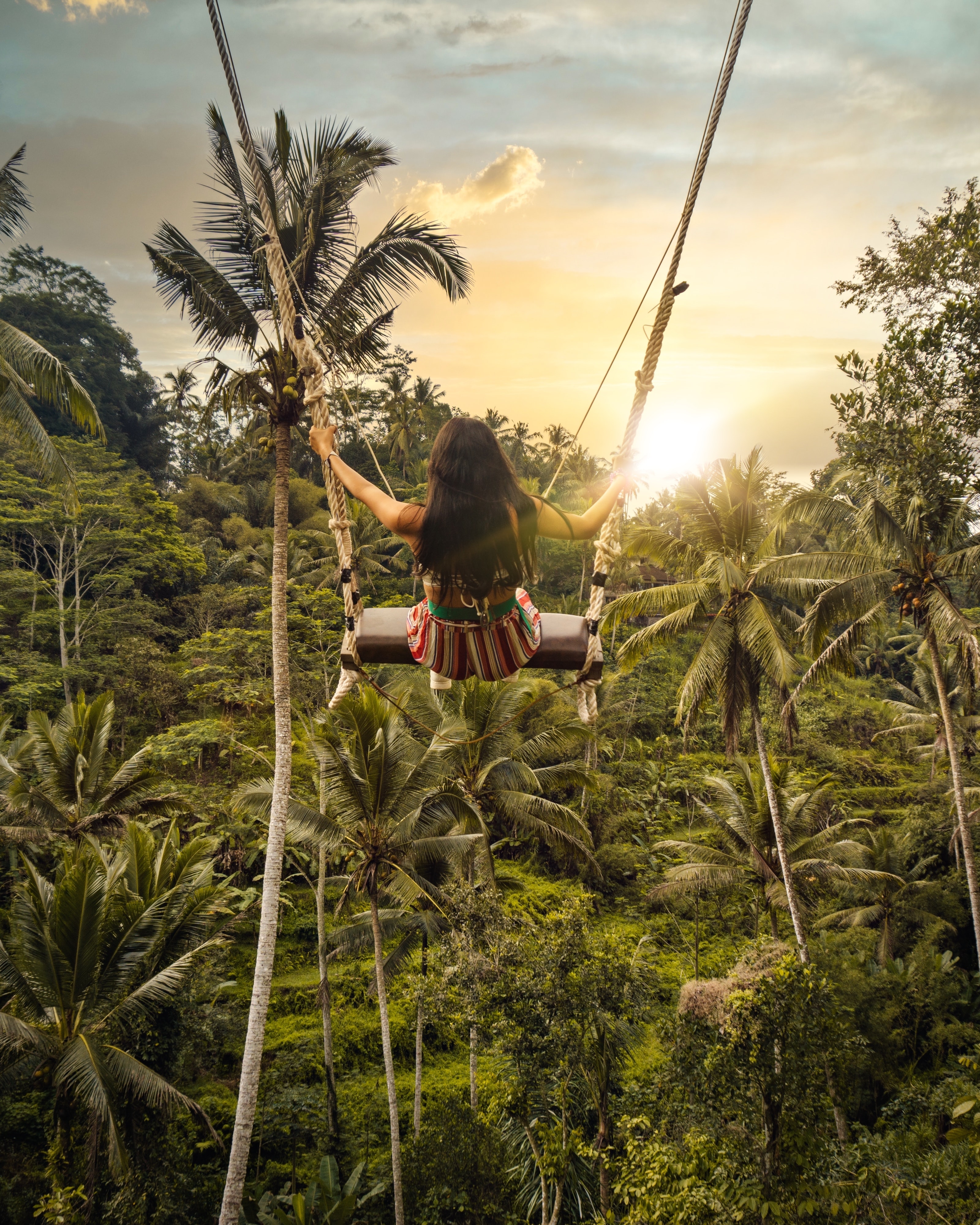 A woman sat on a swing over a dense jungle
