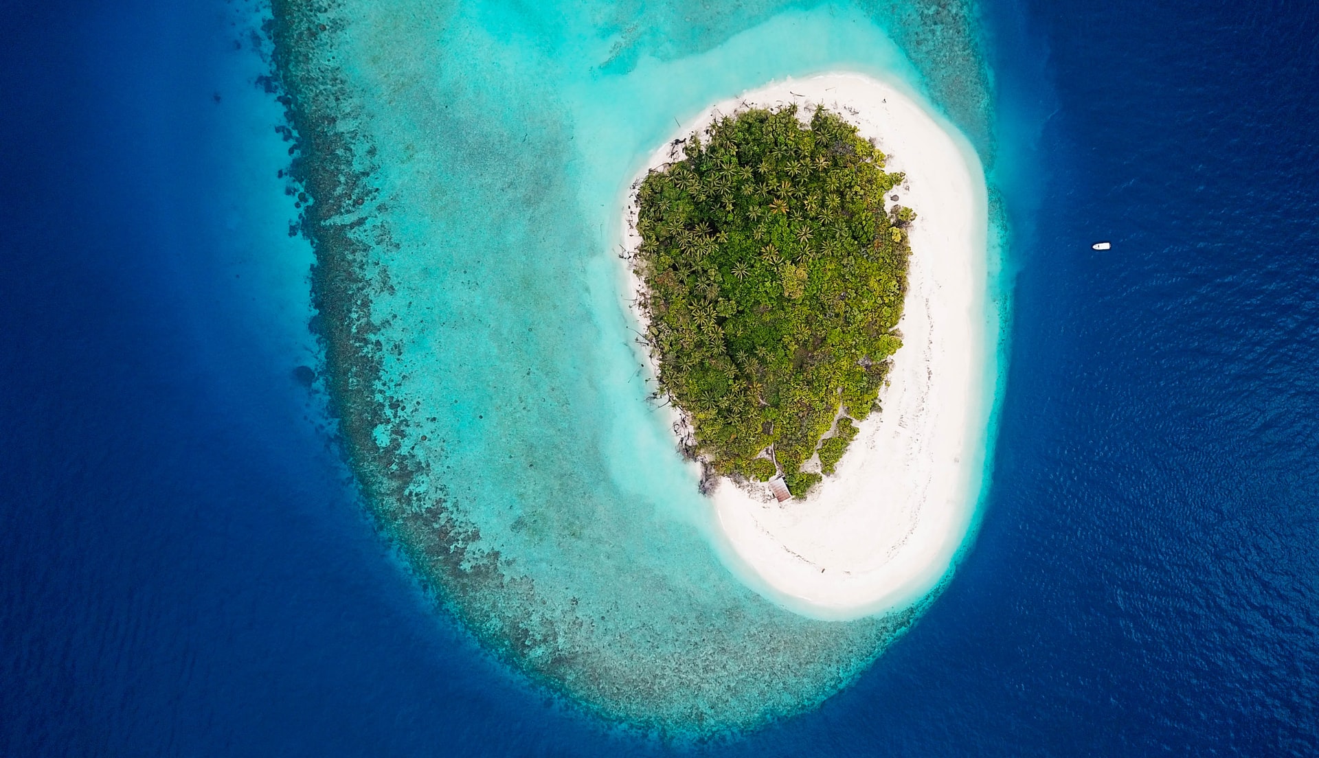 Aerial view of tiny island encircled by waters of different blue shades