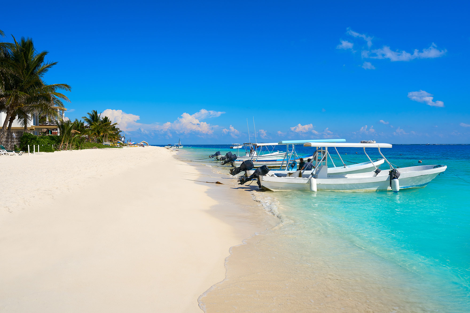 3 small fishing boats docked on a picturesque white sand beach with clear blue waters