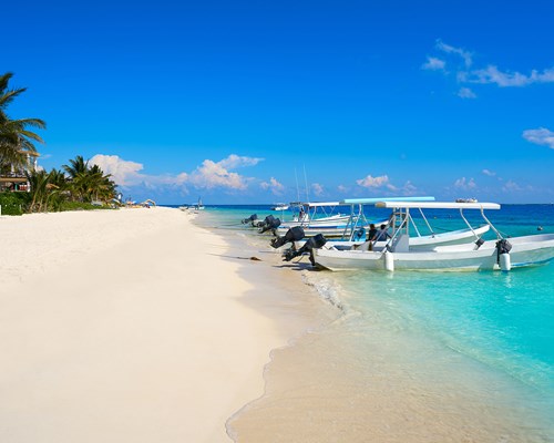 3 small fishing boats docked on a picturesque white sand beach with clear blue waters