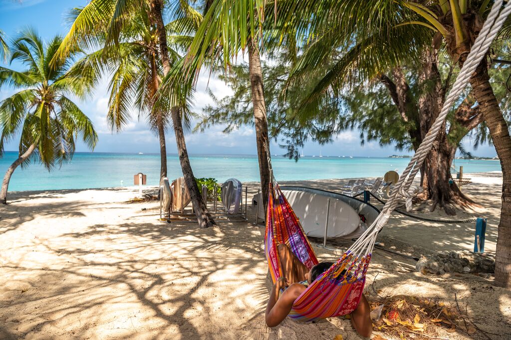 Woman hanging in hammock on white beach with palm trees 