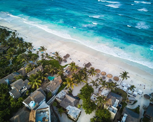 Aerial view of small straw roofed buildings along a stretch of a white sand beach