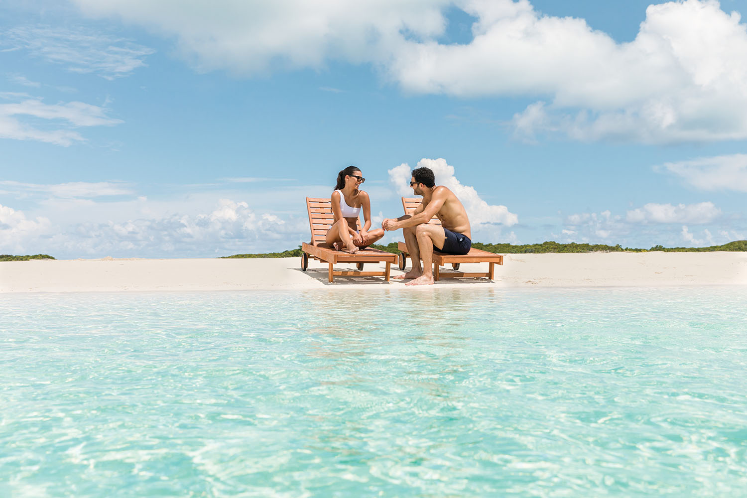 Couple sitting on beach loungers whilst holding hands on a white sand beach