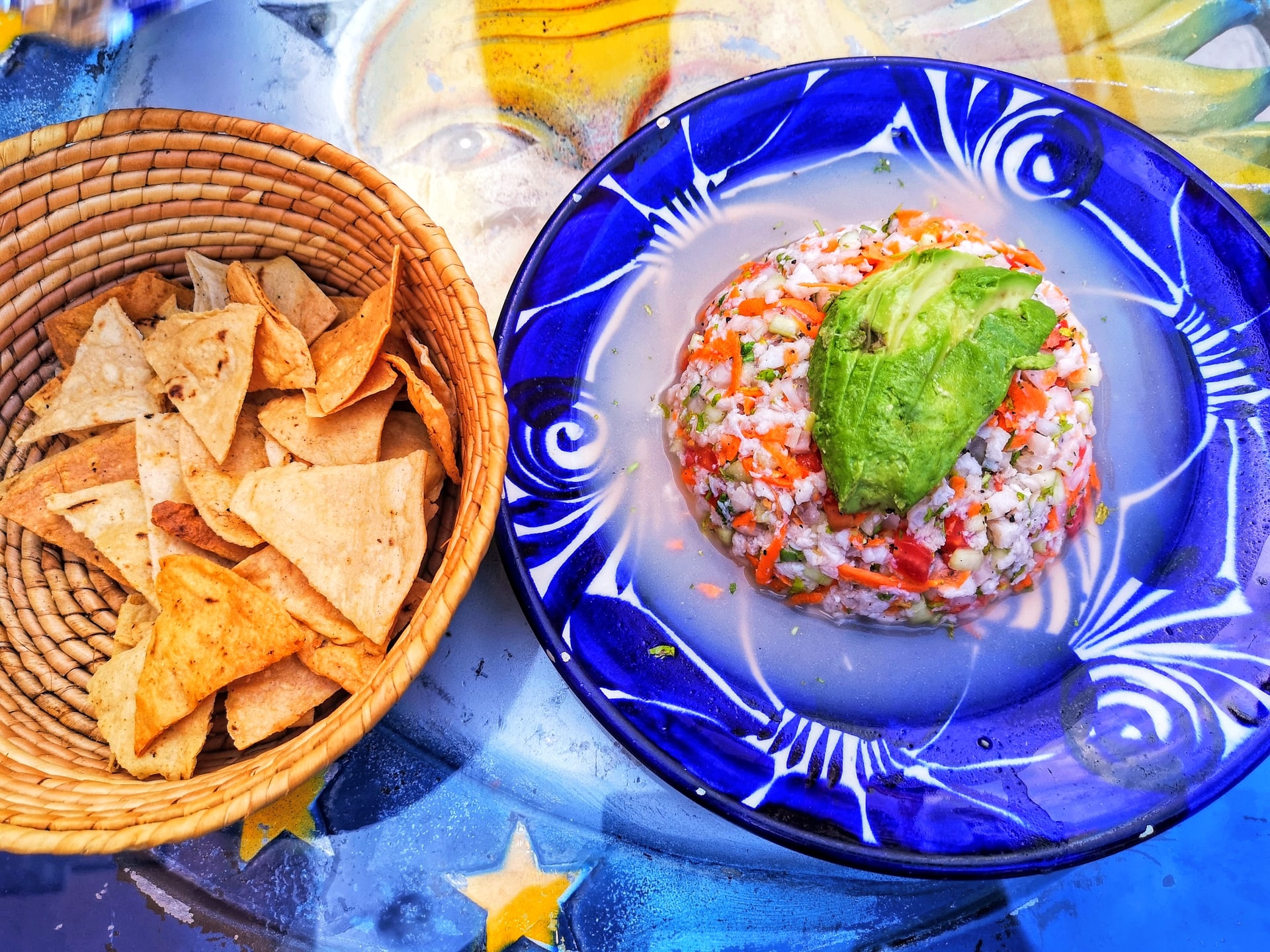 Basket of nachos and colorful salsa with chopped avocado on a blue plate