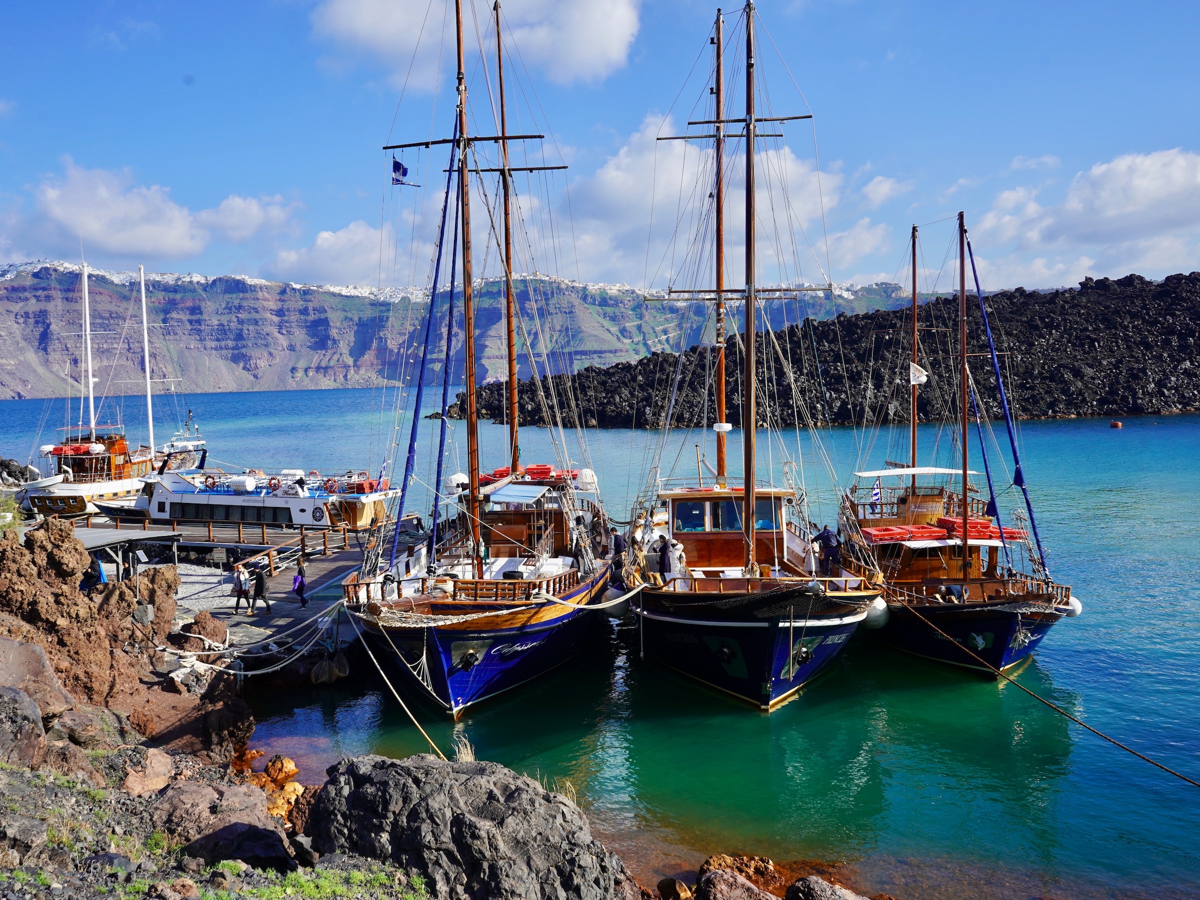Three boats docked on a mint-green lagoon, surrounded by mountain ridges
