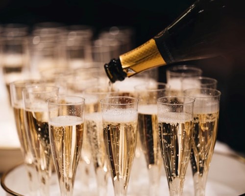 Full glasses of champagne on a tray with a bottle pouring champagne into a glass