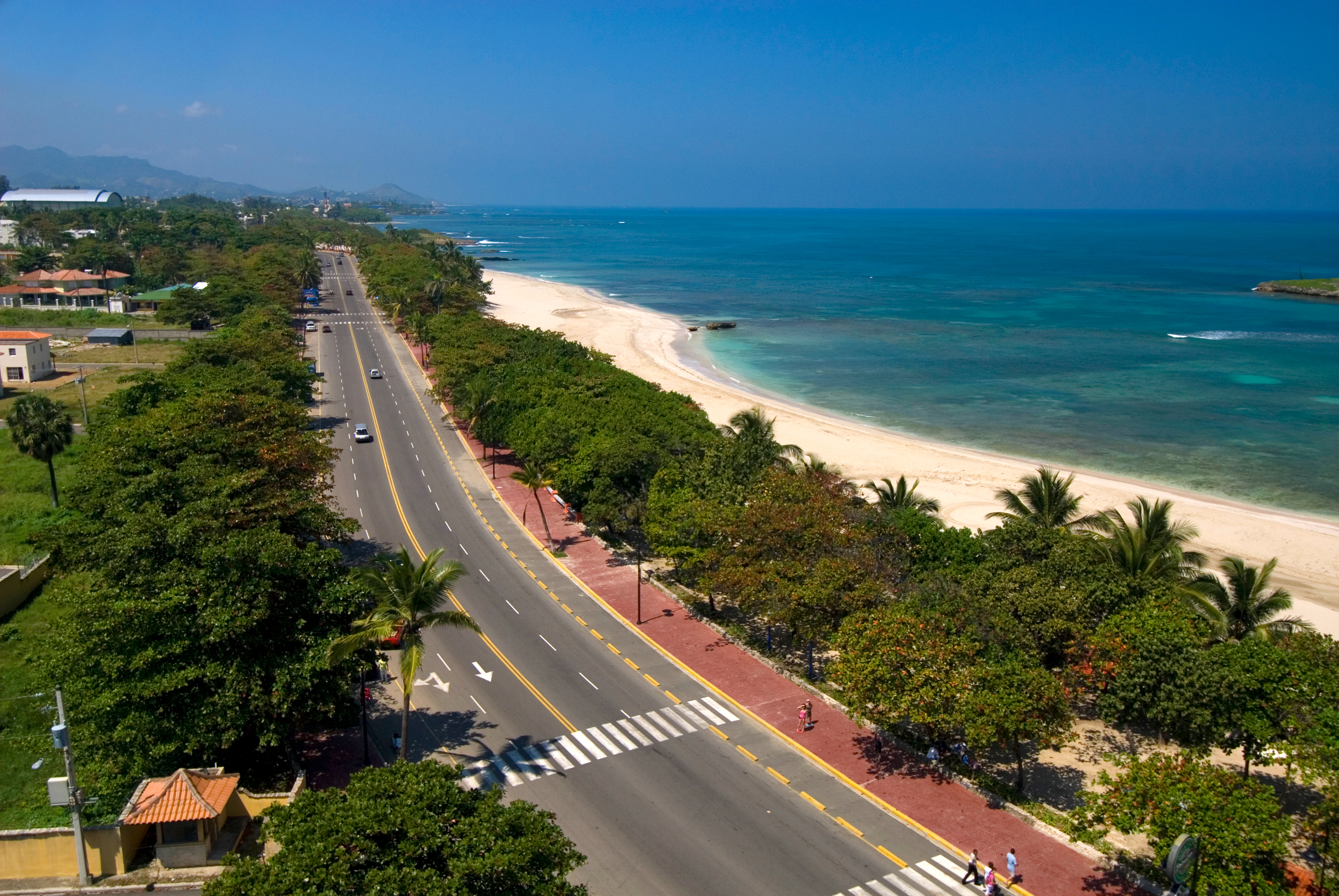 A main road parallel to a tropical beach with white sand and bright blue sea