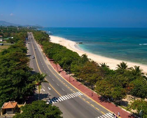 A main road parallel to a tropical beach with white sand and bright blue sea
