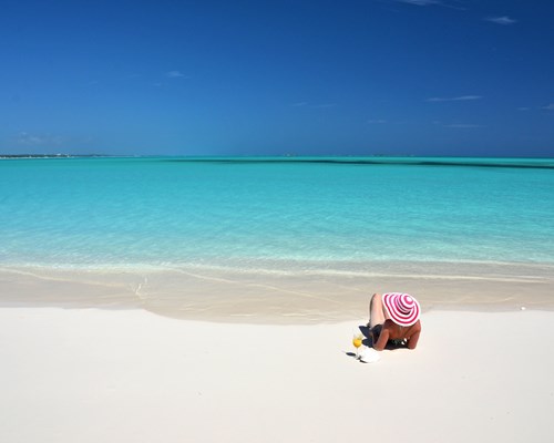 Woman with orange drink laying on white sand beach in the Bahamas