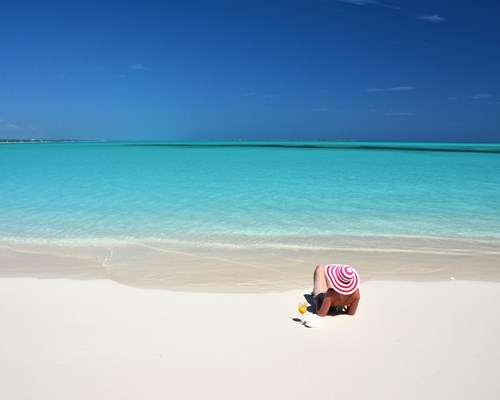 Woman with orange drink laying on white sand beach in the Bahamas