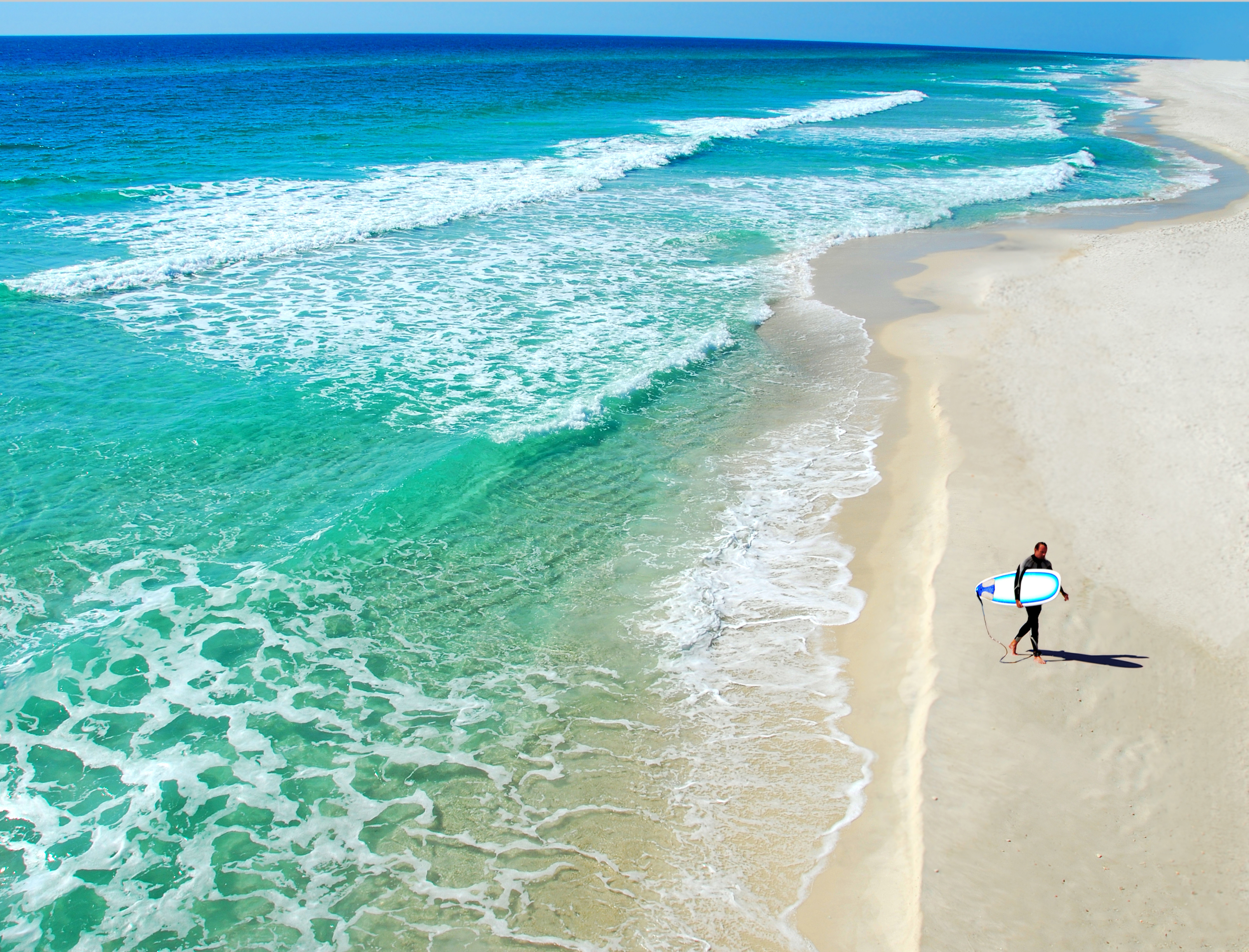 Lone surfer holding a surf board on a tropical beach 
