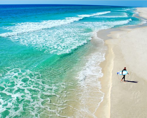 Surfer walking along pristine beach with a surfboard