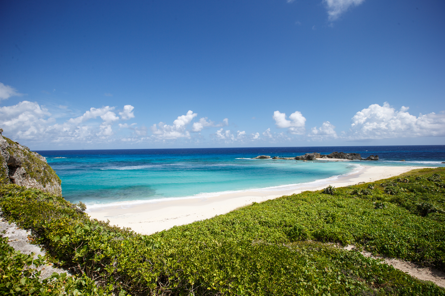 View of a tropical beach with pristine white sand beach, blue sea and several rocks heading into the sea