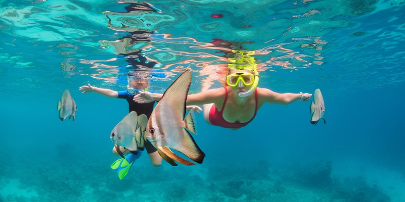 Mother and kid snorkelling with tropical fish