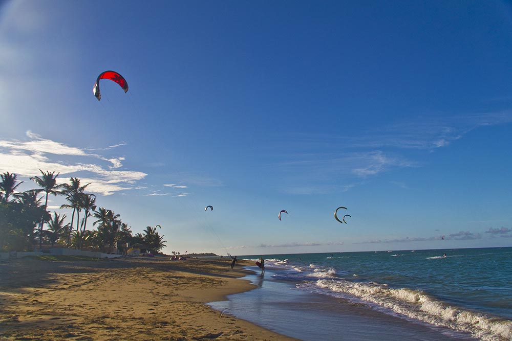 Windsurfers and kitesurfers on a tropical beach with golden sand and choppy blue sea