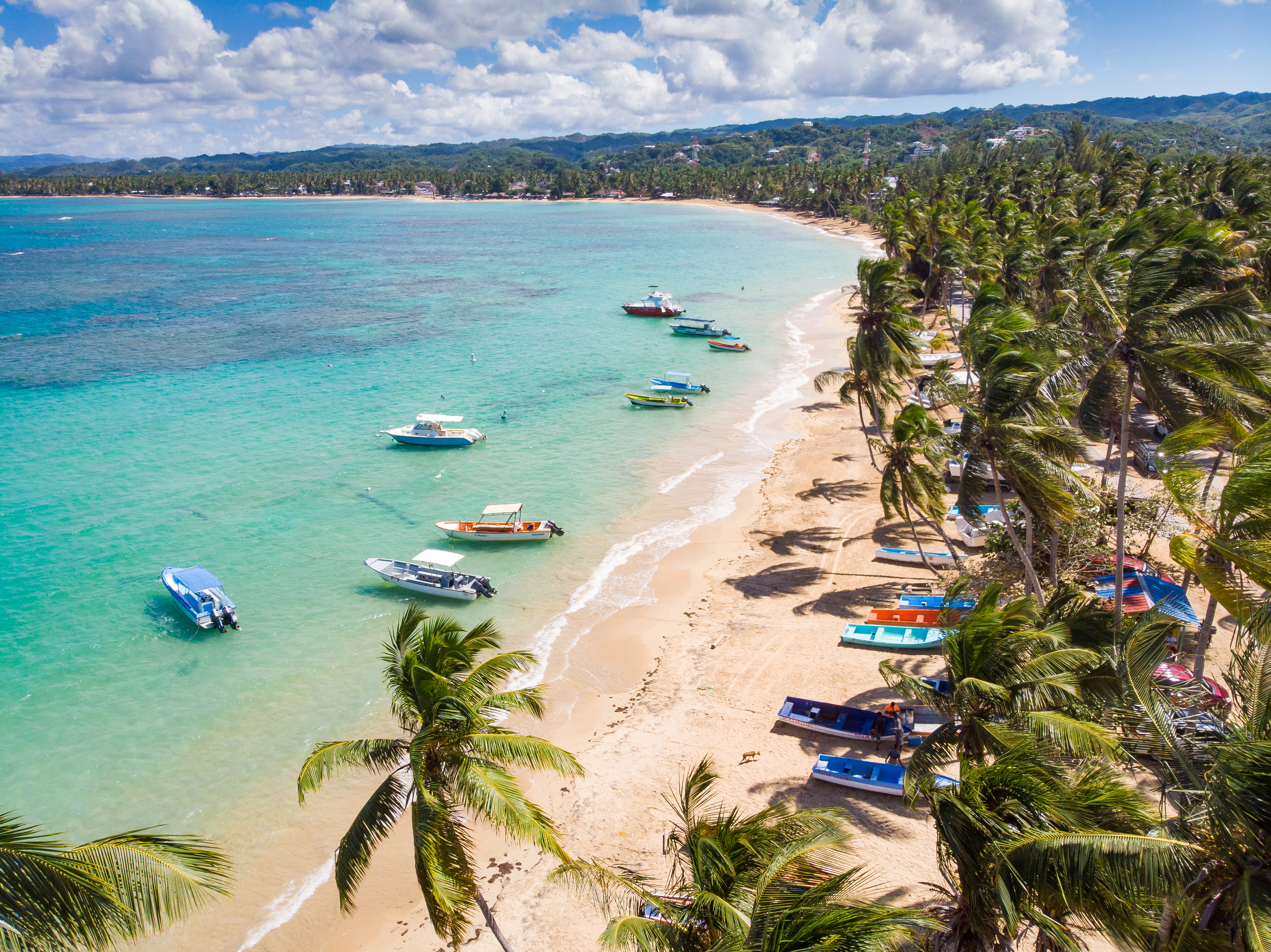 Aerial view of small boats docked up on a tropical beach with golden sand and bright turquoise sea 
