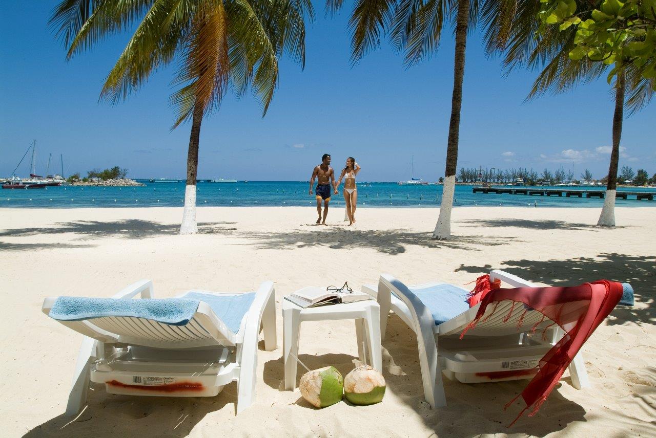 A couple walking back to their loungers on a pristine white sand Caribbean beach 