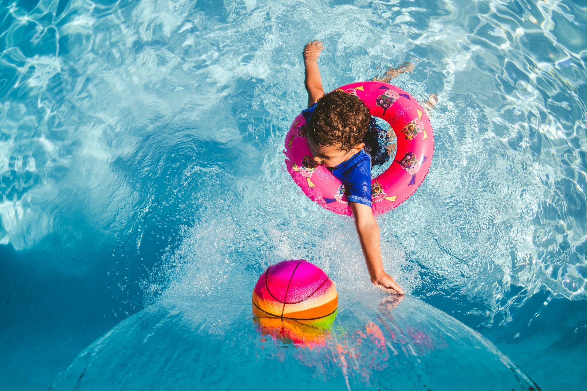  Child in blue top swimming in pool with pink rubber ring 