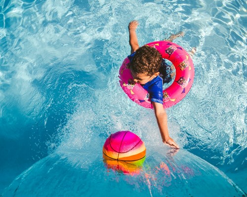 Child in blue top swimming in pool with pink rubber ring