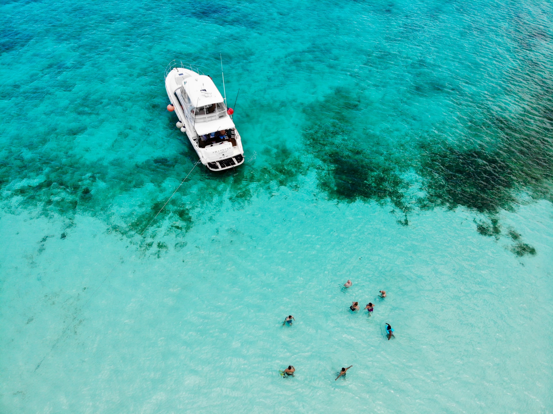 Aerial view of people swimming in shallow tropical sea near a white boat