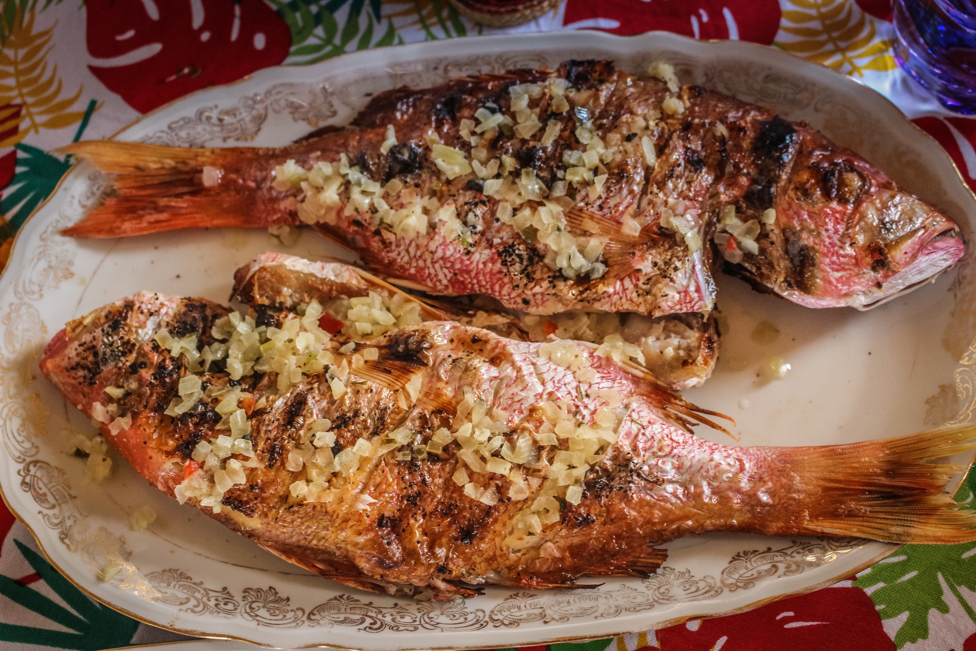 Two fried fish covered in pieces of garlic on a white plate