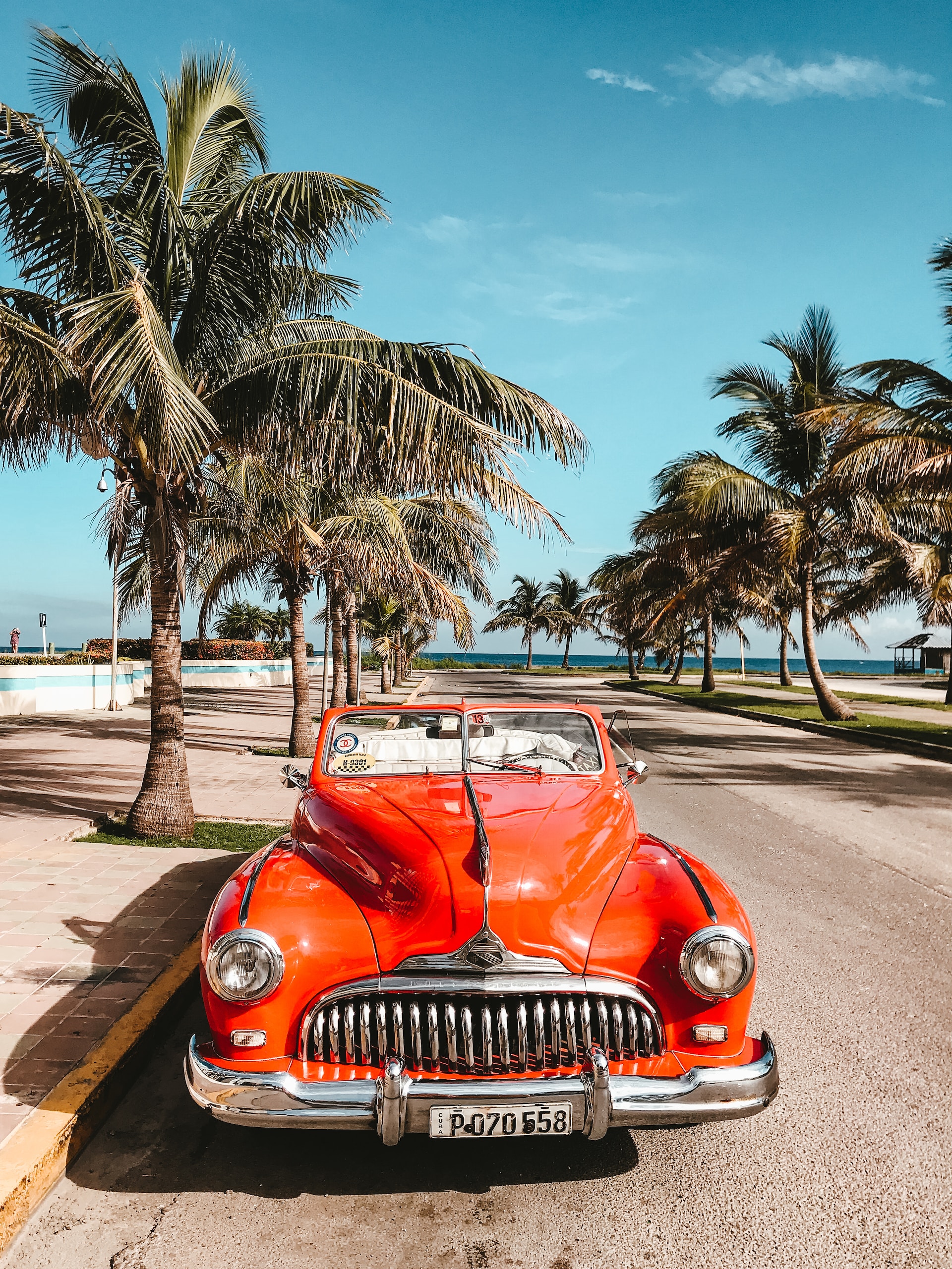 A red car parked on the road with palm trees