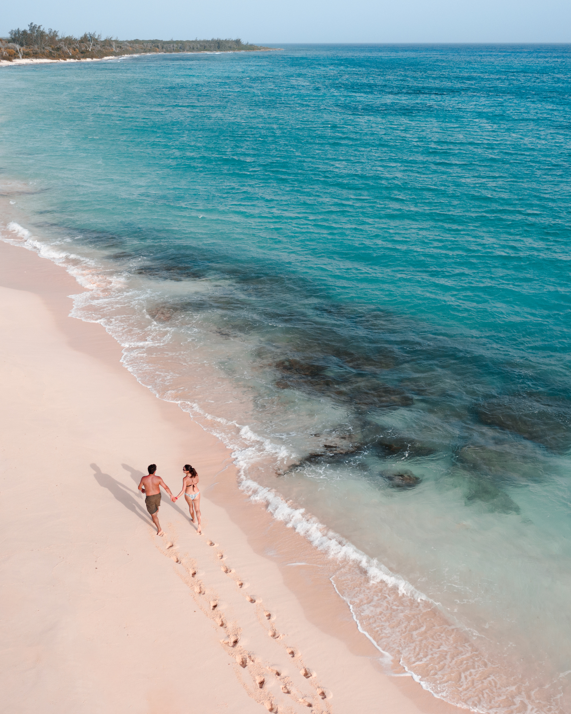 Couple walking on serene beach leaving trail of footprints behind with diamond blue ocean