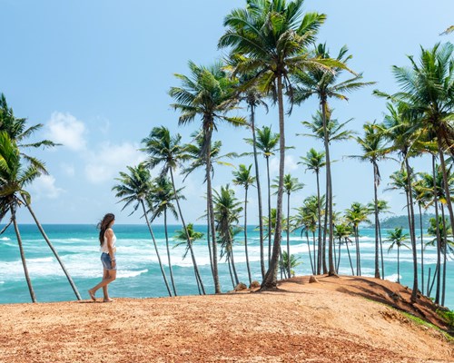 Woman walking along small sandy ledge next to a wavy sea