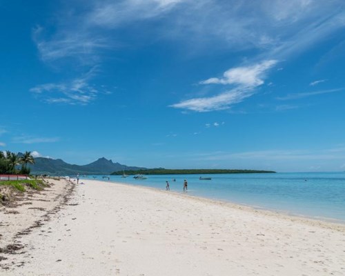 Wide, sandy beach with people in the sea and mountain in the background
