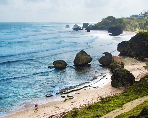 Aerial view of 2 surfers walking along a tropical beach