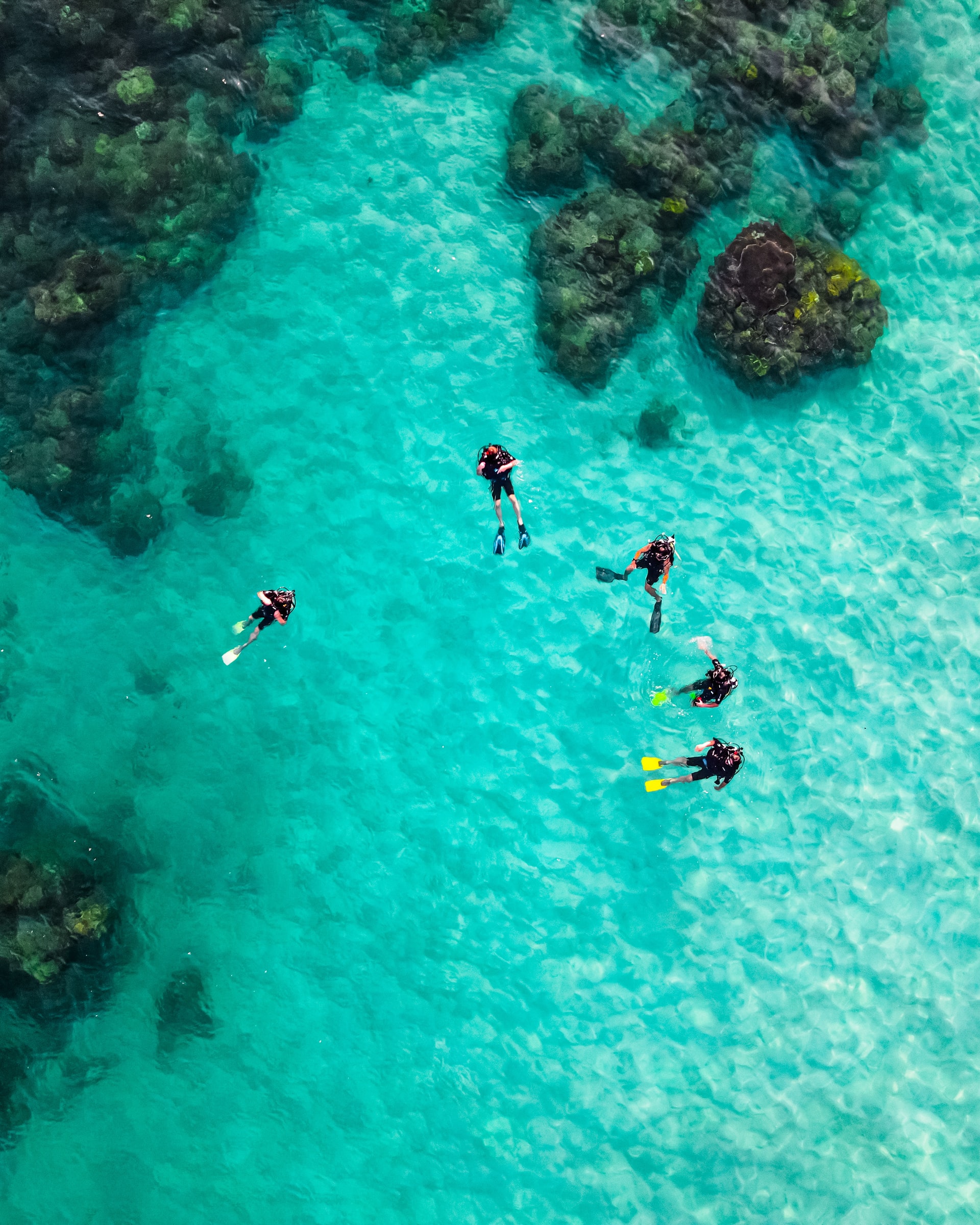 Aerial shot of a group of scuba divers near some rocks in clear bright blue sea