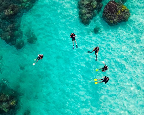 Five people bathing in a body of water surrounded by rocks