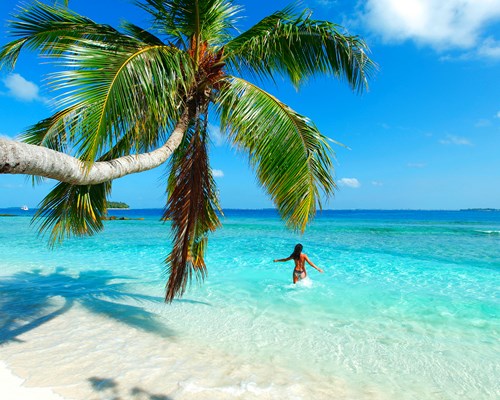 Woman with her arms out splashing around in turquoise sea in a sunny destination