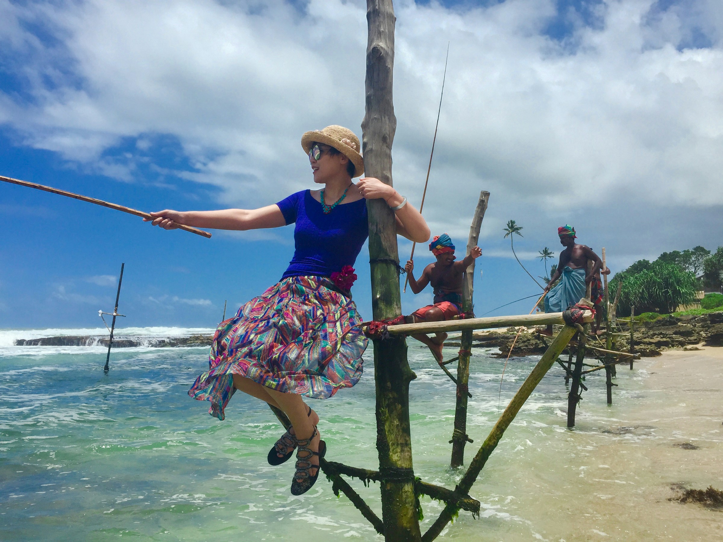 A woman and locals fishing on stilts at a beach in Sri Lanka