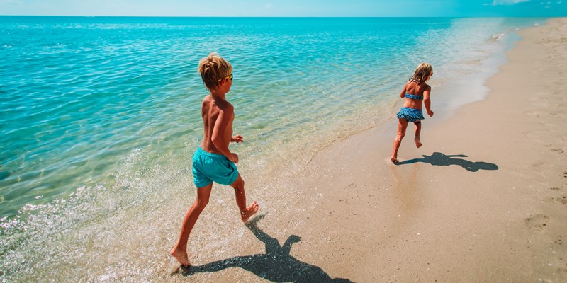 Small girl and boy run in calm sea along edge of sandy beach