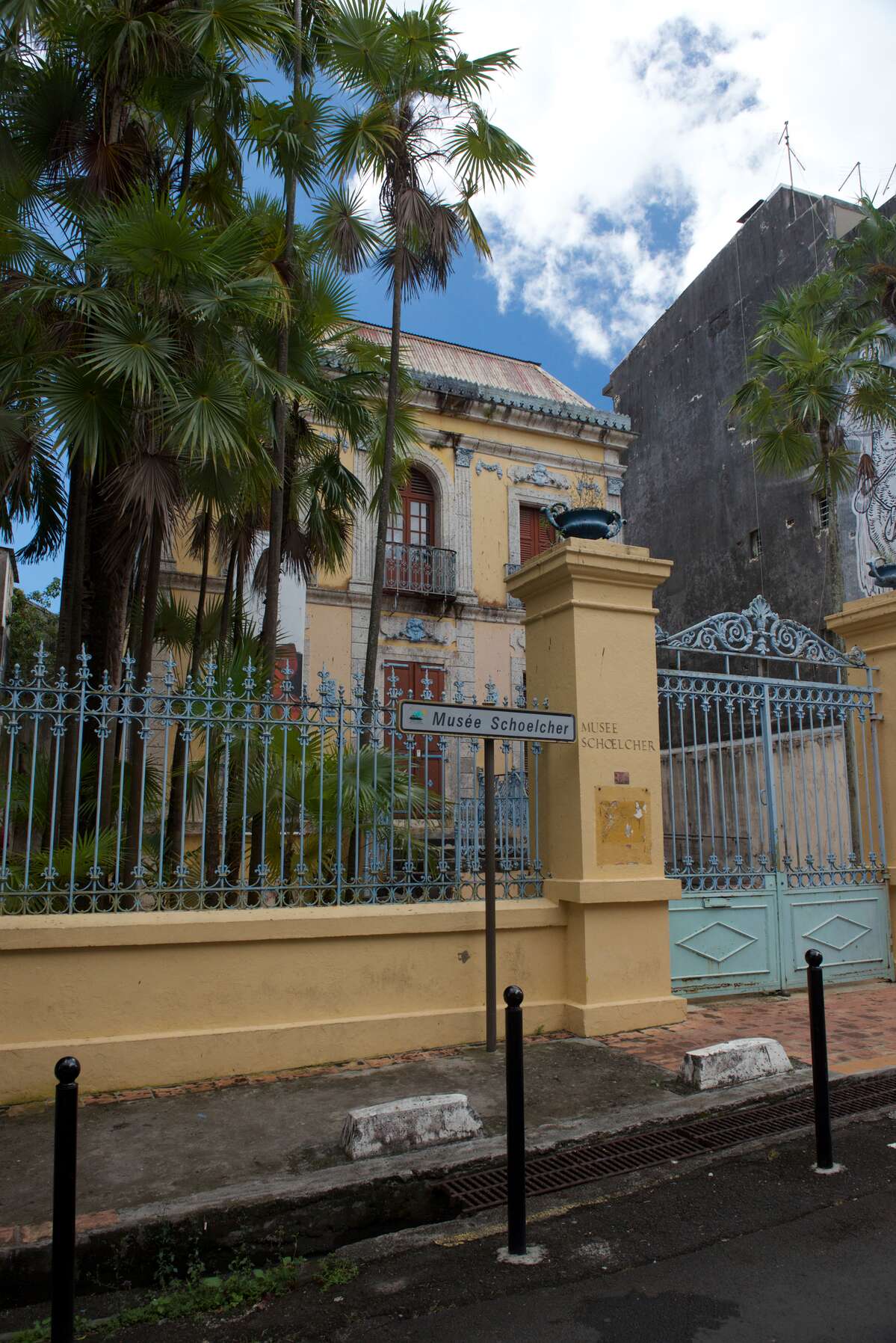 Exterior view of a grand yellow building with tall tropical trees