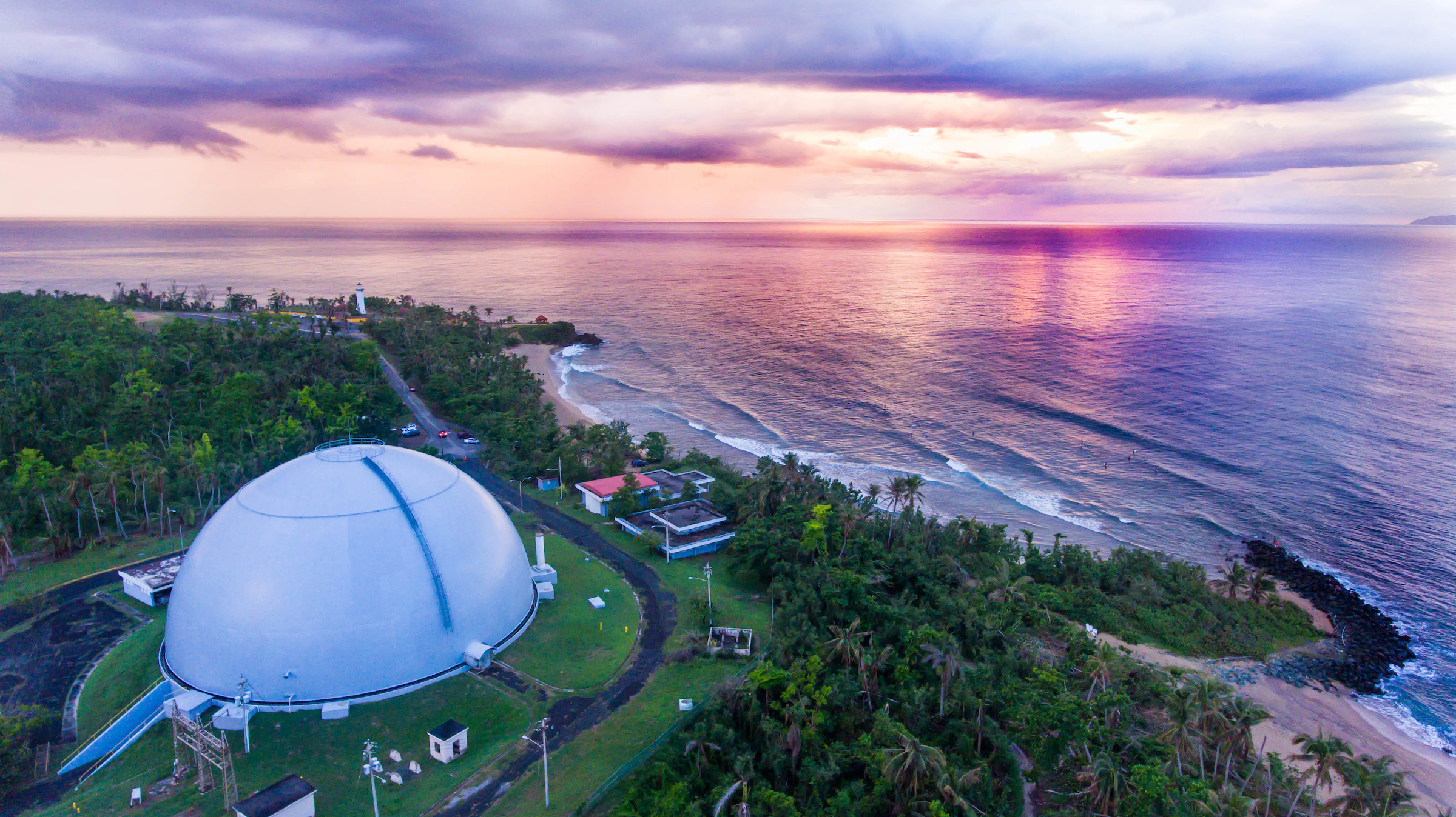 Dome surrounded by palm trees with lilac sunset skies meeting with ocean