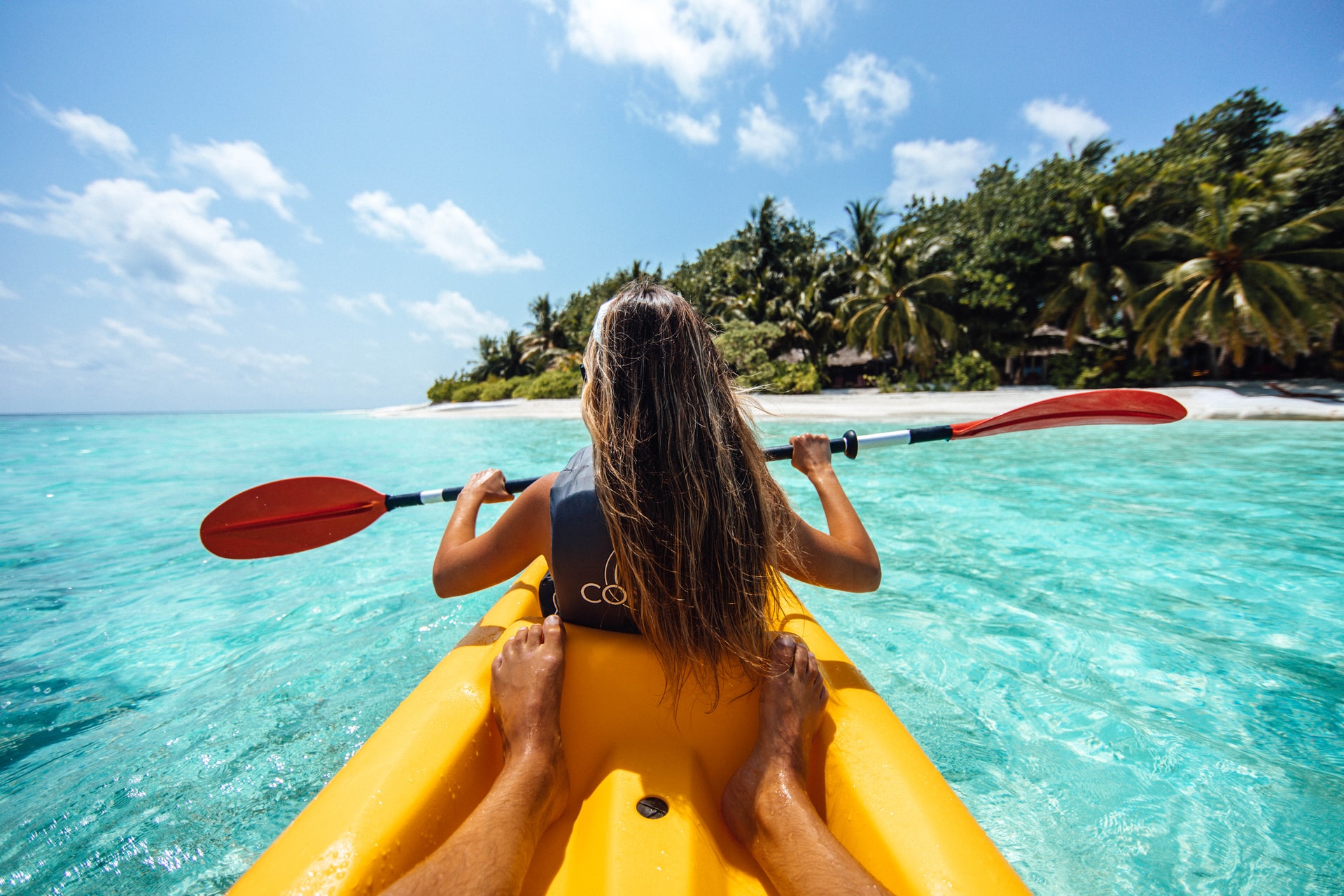 Woman kayaking towards a lush green island over turquoise ocean
