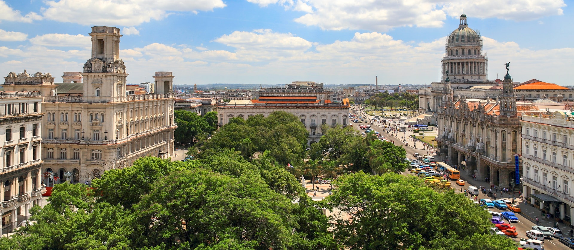 Tall ornate buildings around a small park with trees in Havana city centre