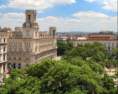 Tall ornate buildings around a small park with trees in Havana city centre