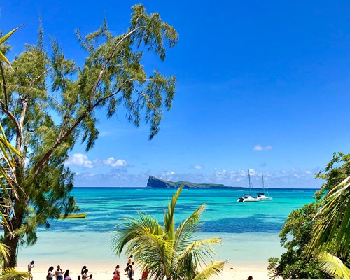 People standing on a white beach with a turquoise sea with boats and small island in the background