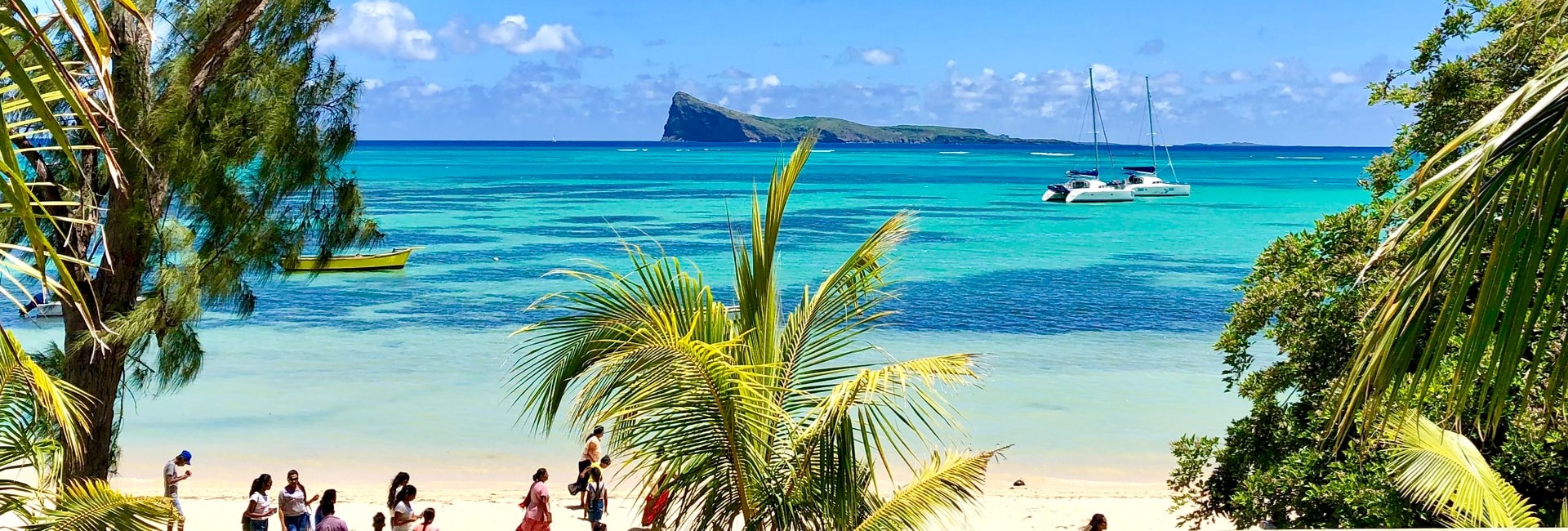 People standing on a white sand beach with a shallow, turquoise sea and small island in the background