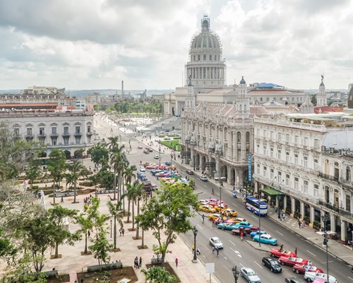 Colourful vintage American cars parked in a row outside of a large old building in Havana city