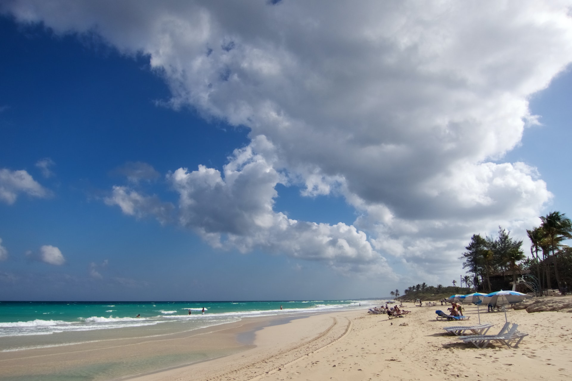 People sitting on sun loungers on a wide white sand beach