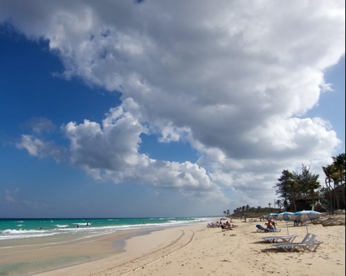 People sitting on sun loungers on a wide white sand beach