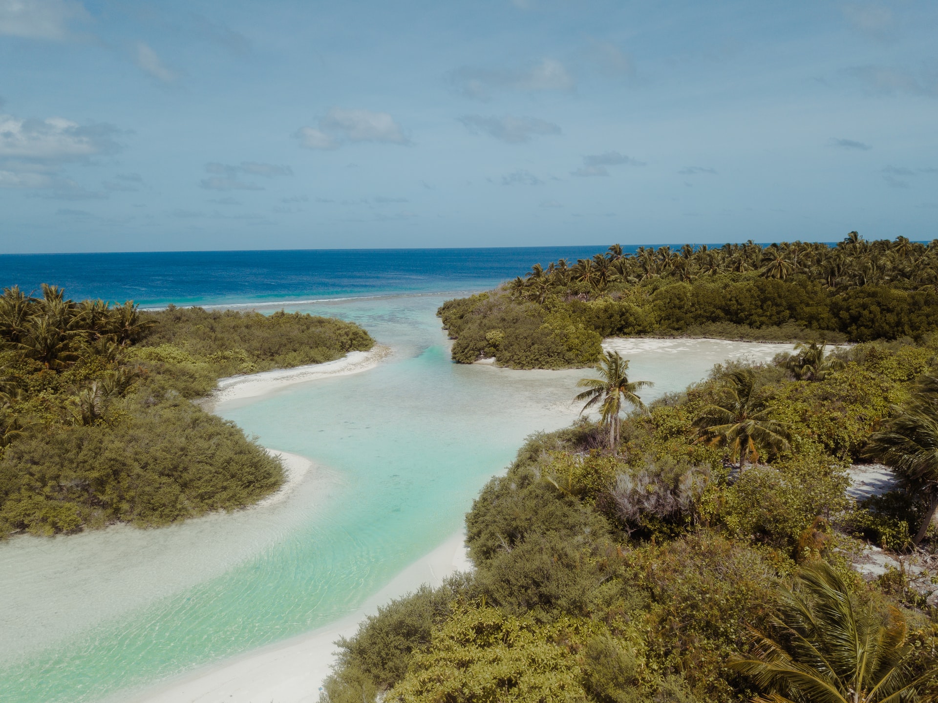 Clear, pale blue river with white sandbanks flowing into tropical sea